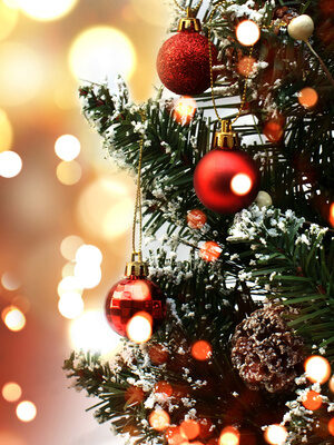 Seitenansicht eines festlich rot geschmückten Weihnachtsbaums mit leuchtenden Lichtern im Hintergrund.